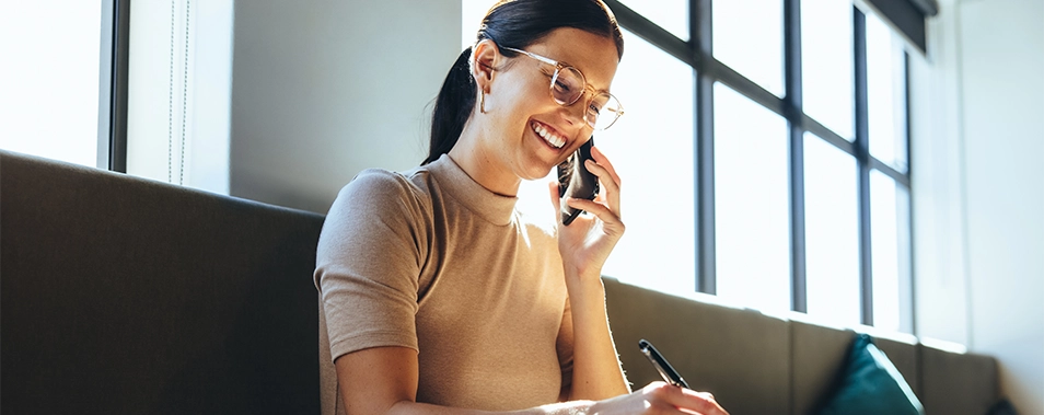Eine Frau lächelt und hält Handy und Stift in der Hand.
